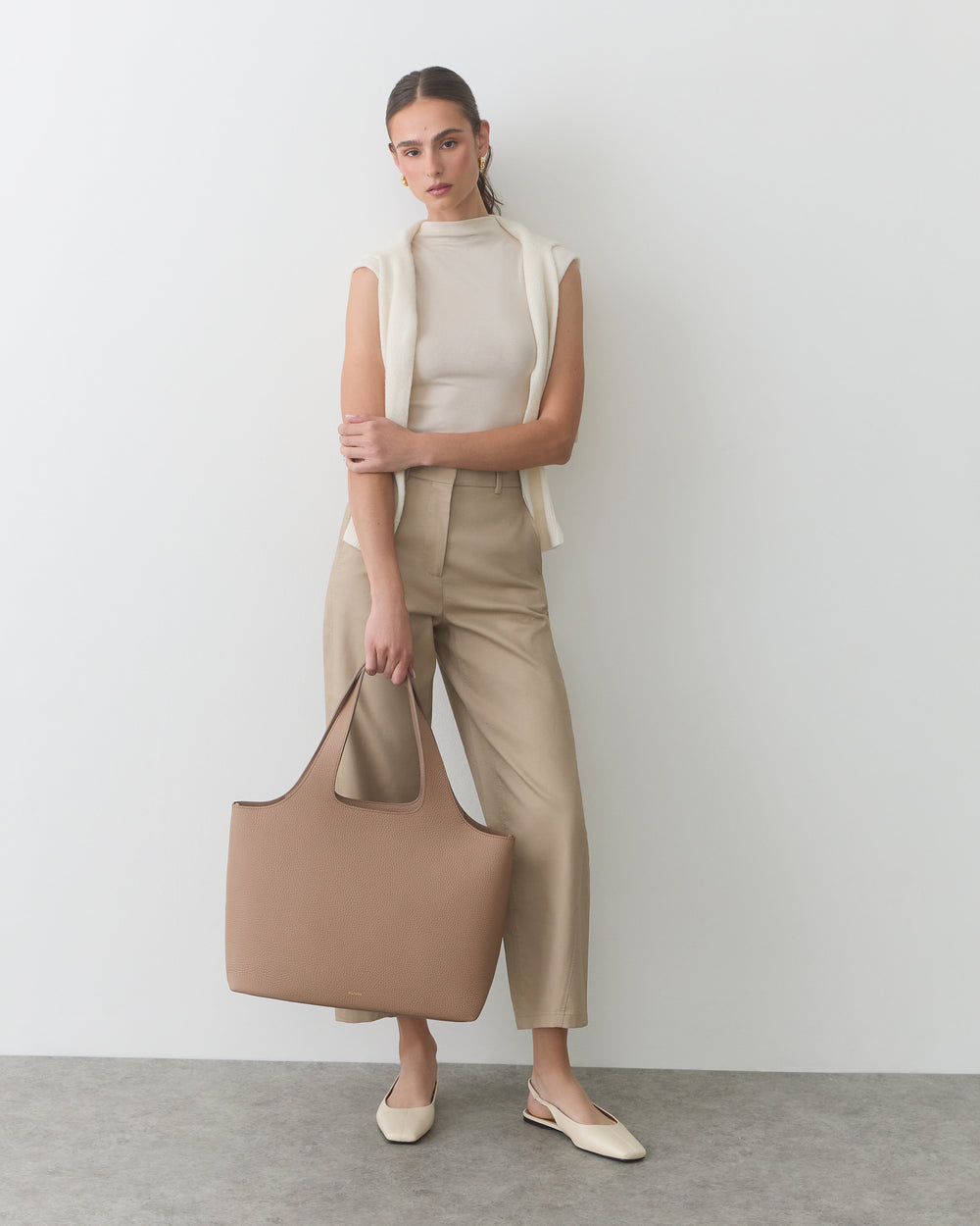 Person holding a large bag, wearing sleeveless top, pants, and slip-on shoes.