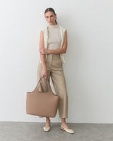 Person holding a large bag, wearing sleeveless top, pants, and slip-on shoes.