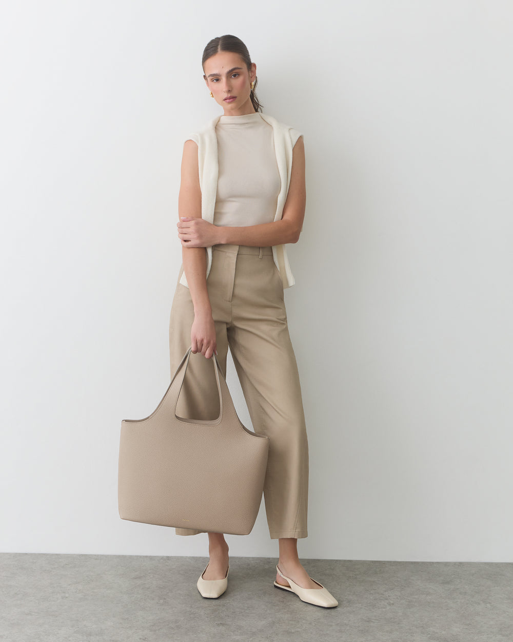 Person in sleeveless top and pants holding a large tote bag.