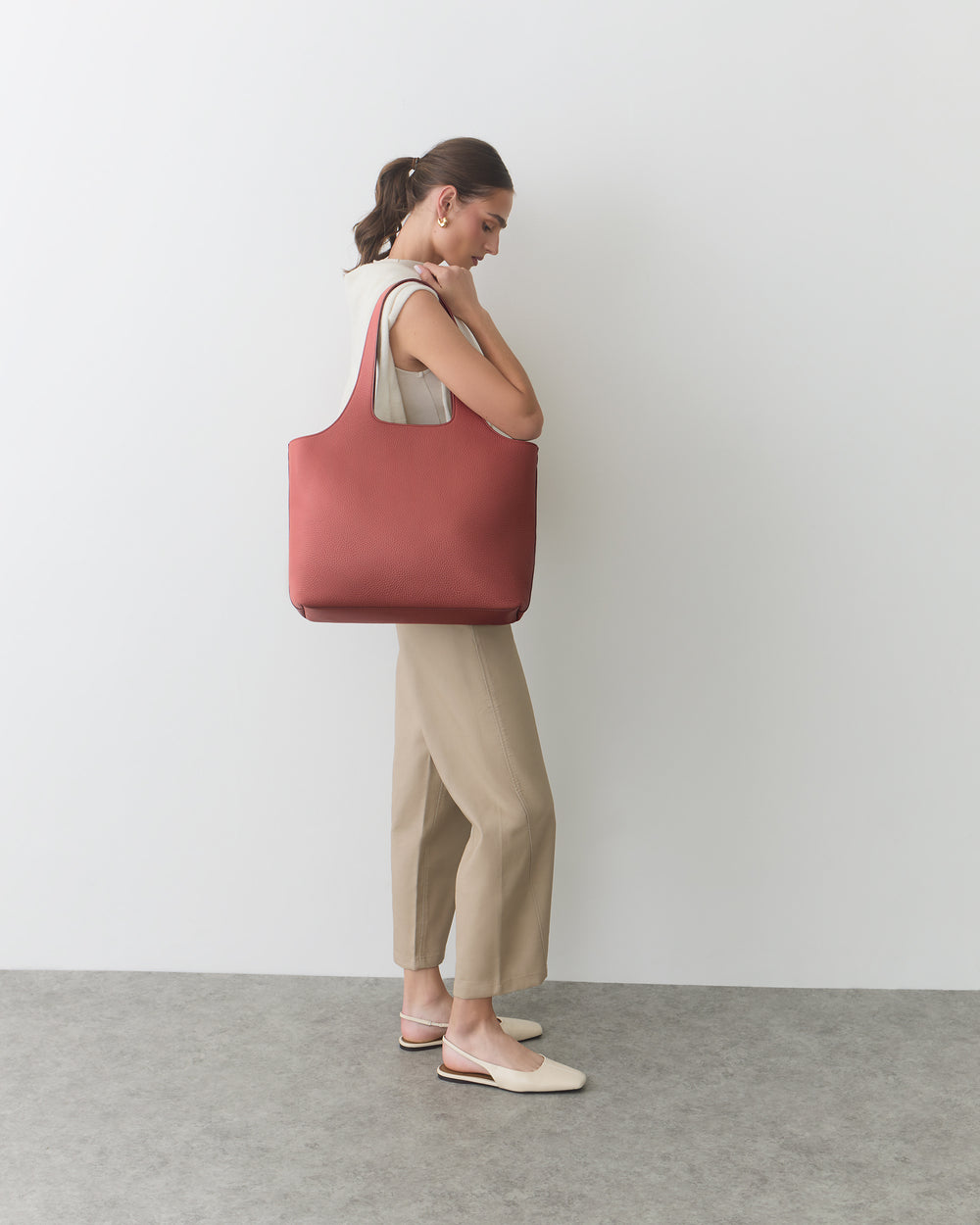 Person standing with large shoulder bag and hands crossed in front.