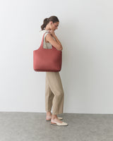 Person standing with large shoulder bag and hands crossed in front.