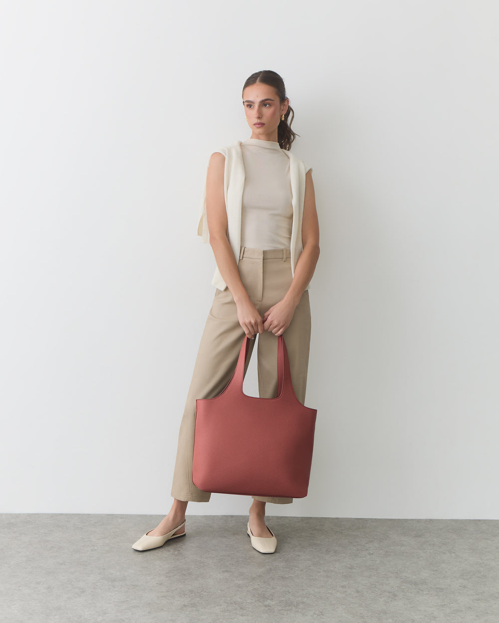 Person standing with a red tote bag, wearing a sleeveless top and pants.