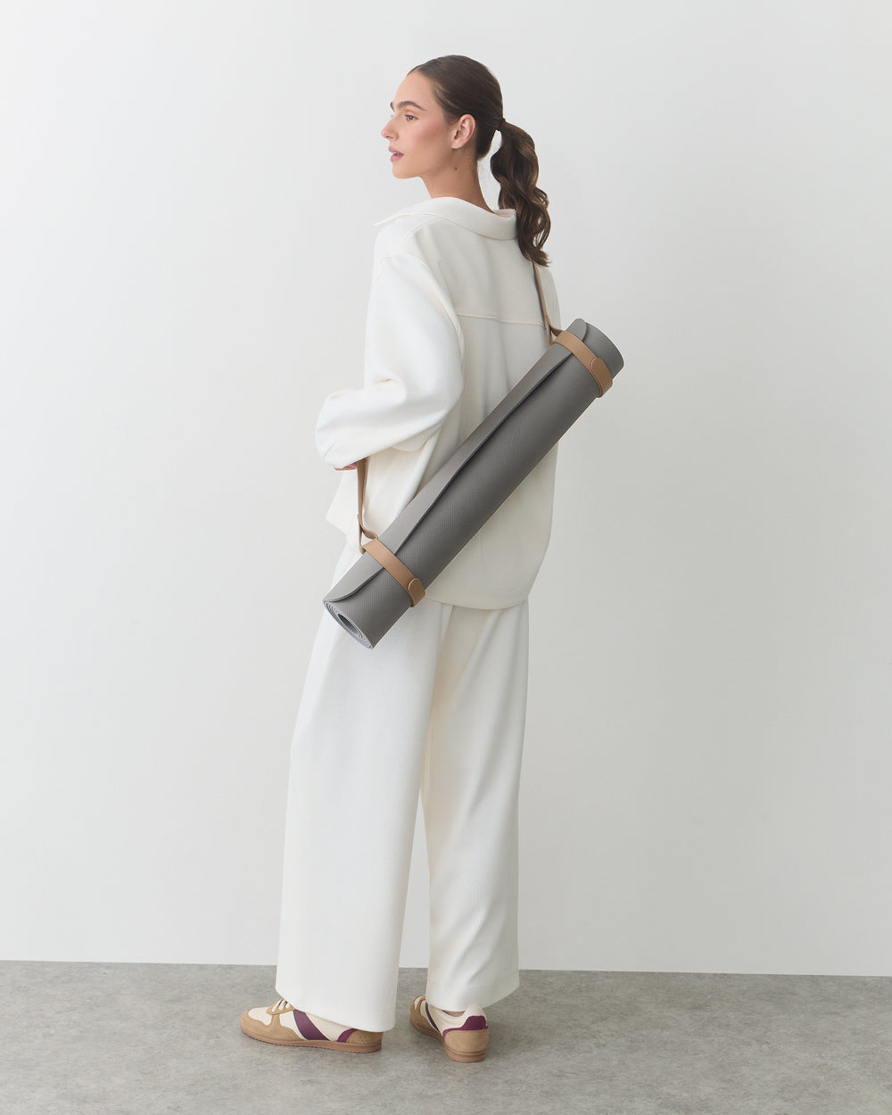 Person standing with a yoga mat bag over shoulder, wearing a matching outfit and shoes.