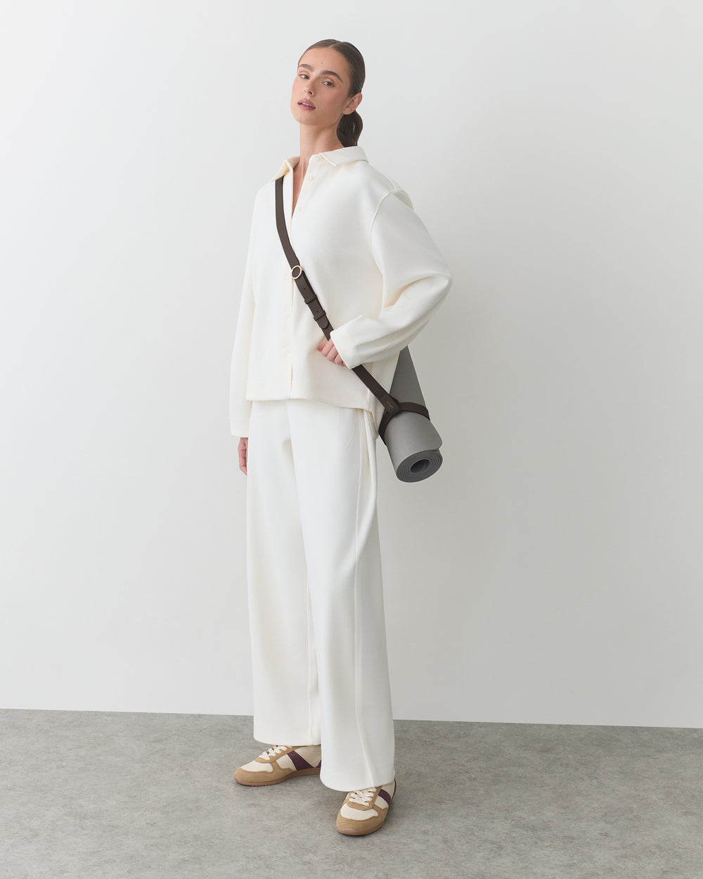 Person in relaxed outfit holding a yoga mat bag over shoulder.