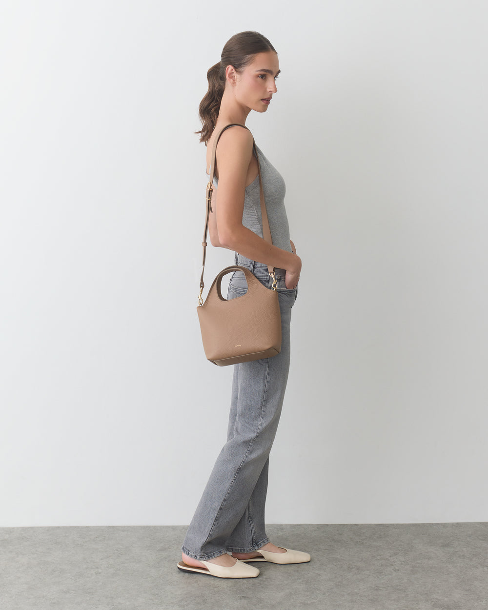 Person standing with handbag over shoulder, wearing a sleeveless top and jeans.