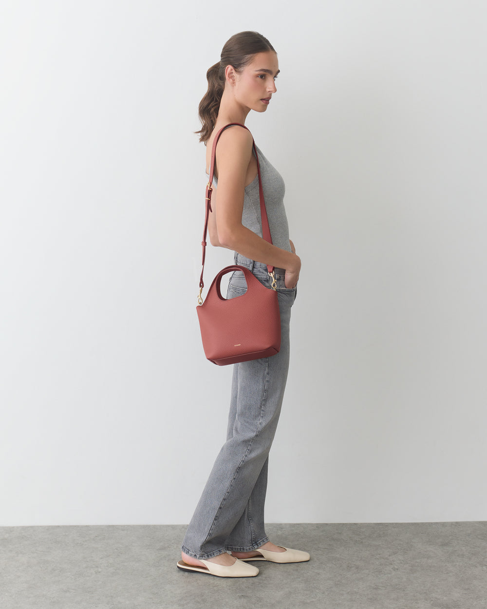 Person standing sideways holding a purse with a shoulder strap.
