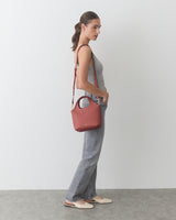 Person standing sideways holding a purse with a shoulder strap.