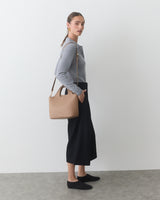 Person standing with shoulder bag, wearing long skirt and sweater.