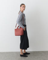 Person standing with shoulder bag wearing long-sleeved top and pants.