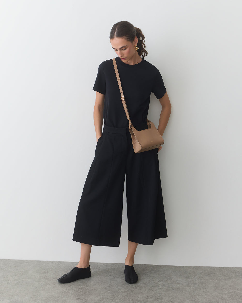 Person wearing a t-shirt and wide-legged pants with a crossbody bag.