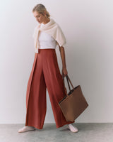 Person holding a tote bag, wearing wide-leg pants and a sweater draped over shoulders.