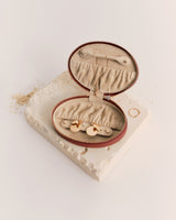 Round jewelry case open on textured surface with gold rings inside.