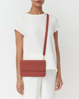 Person with crossbody bag over shoulder, wearing a short-sleeve shirt and pants.