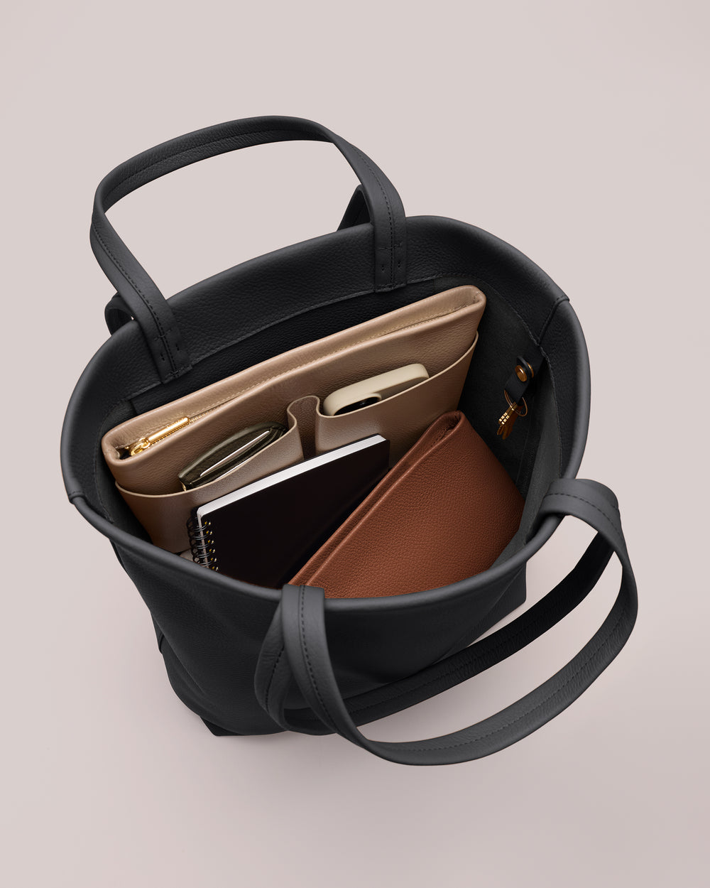 Open tote bag with items like a laptop, notebook, and a pouch inside.