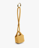 Small textured handbag with a long strap and circular metal handle.