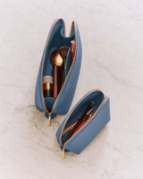 Two open pouches with makeup brushes and cosmetics on a marble surface.