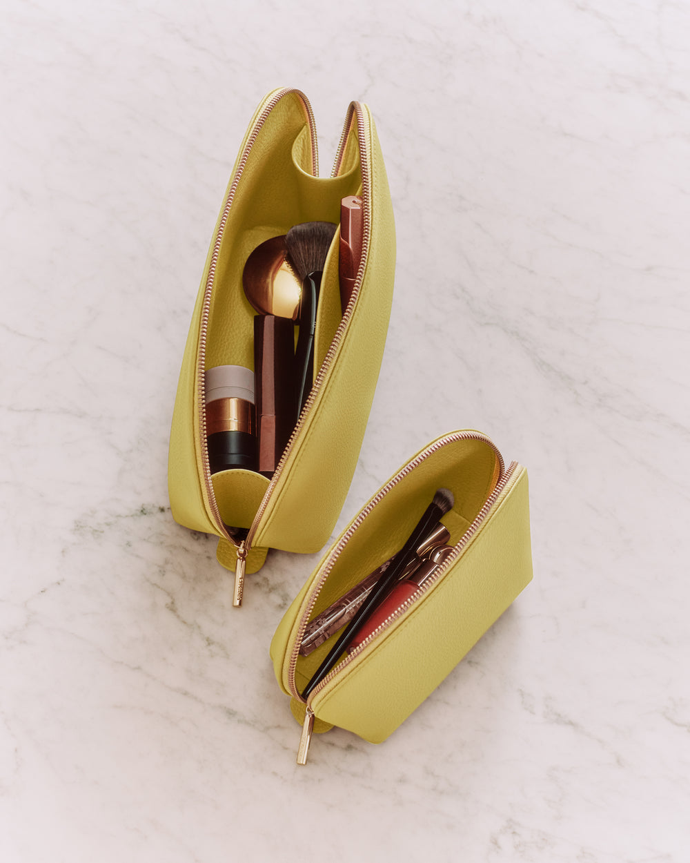 Two open makeup bags with cosmetics on a marble surface.