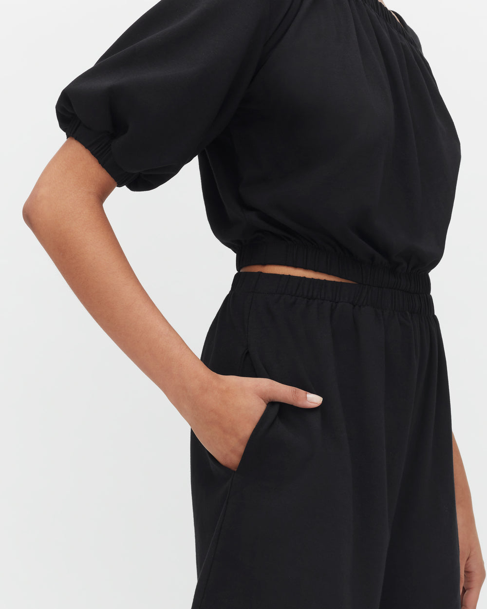 Person wearing a short-sleeve top and pants with a hand in the pocket.