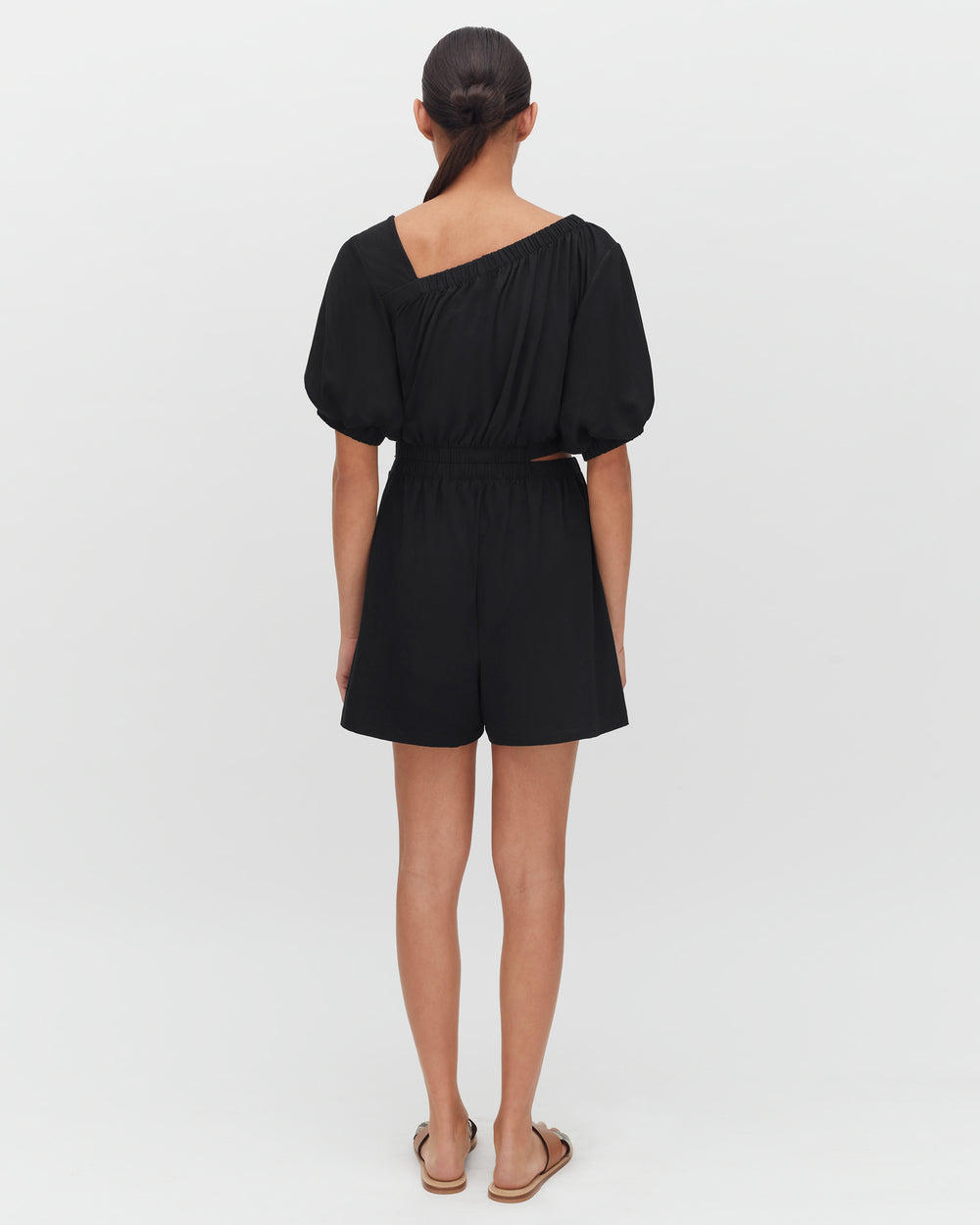 Person in a one-shoulder romper and sandals, facing away.