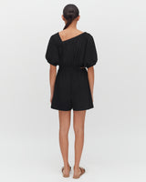 Person in a one-shoulder romper and sandals, facing away.