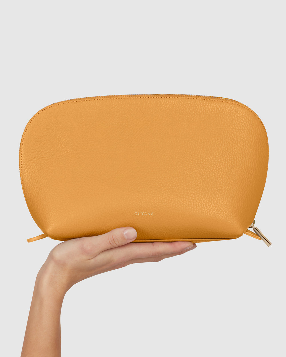 Hand holding a textured, oval-shaped pouch against a plain background.