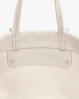 Close-up of a tote bag with two handles and gold rivet details.