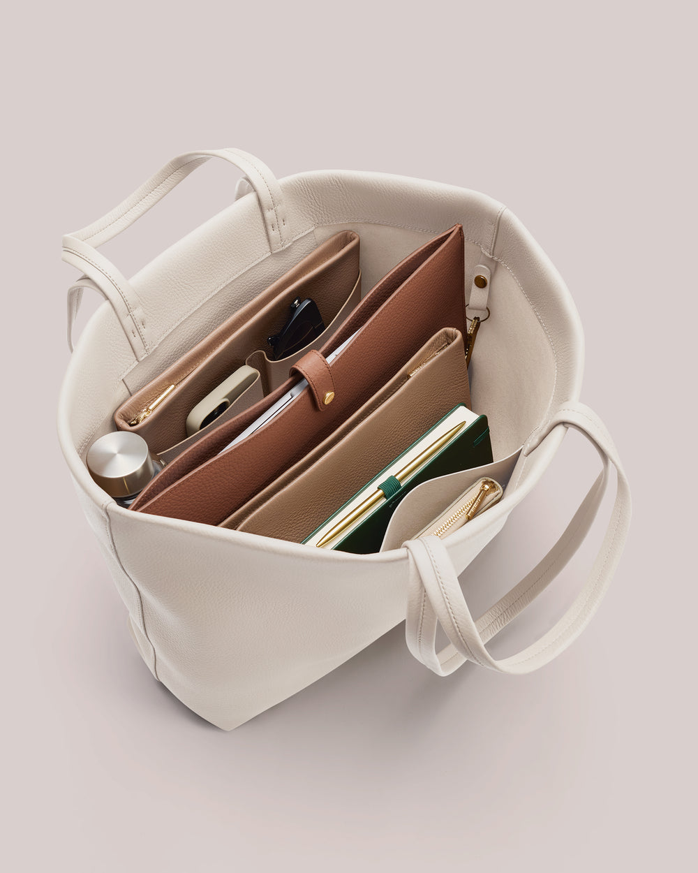 Open tote bag with various items inside including pouches and a notebook.