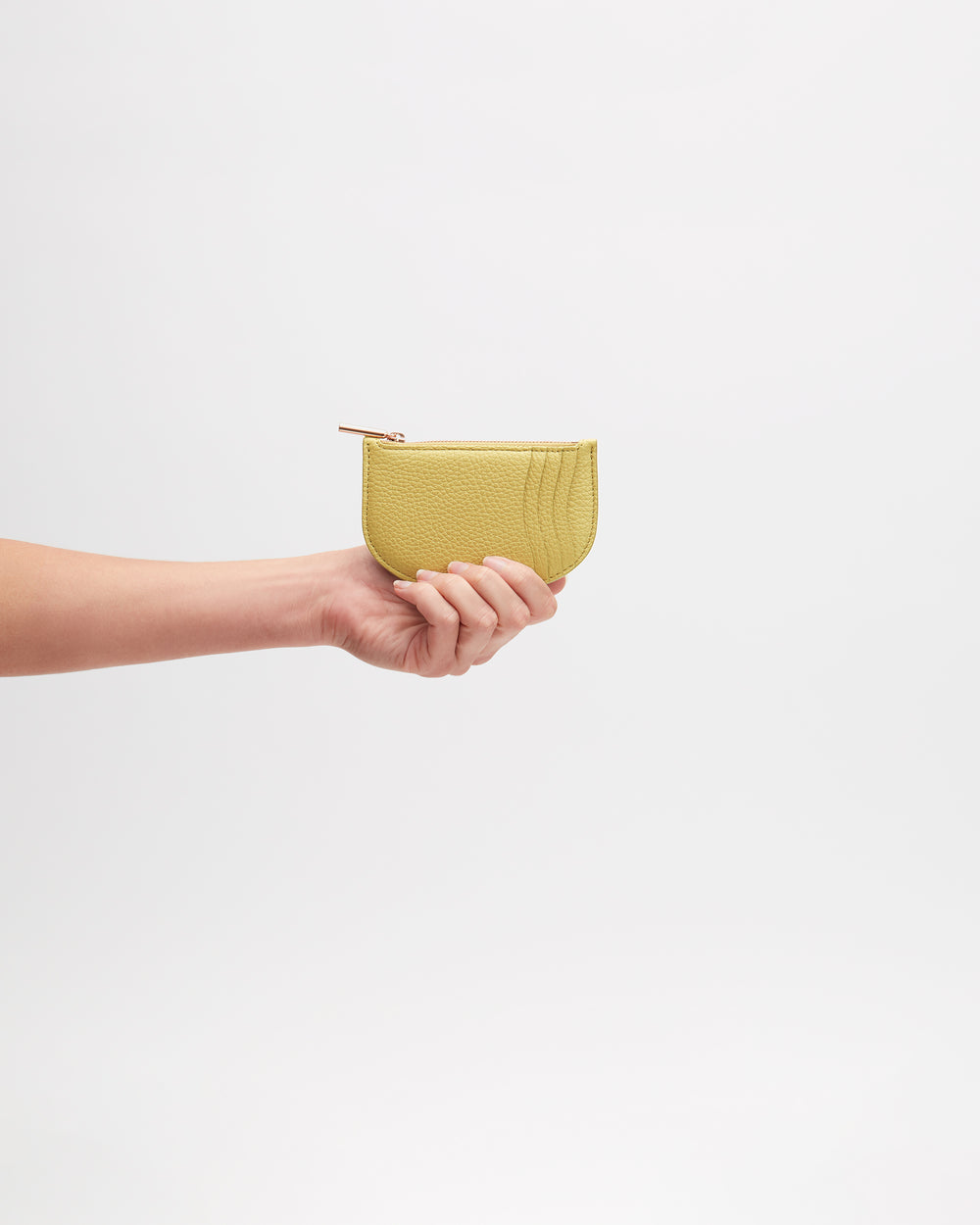 Hand holding a small zippered pouch against plain background.