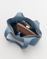 Open tote bag with wallet, phone, and earbuds inside.