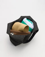 Open tote bag with folded towel, straw hat, and brown pouch inside.