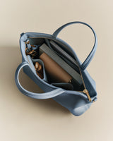 Top view of an open handbag with books and a bottle inside.