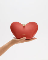 Heart-shaped bag held in a hand against a plain background.