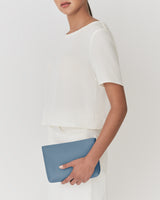 Person holding a rectangular clutch wearing a short-sleeve top and pants.