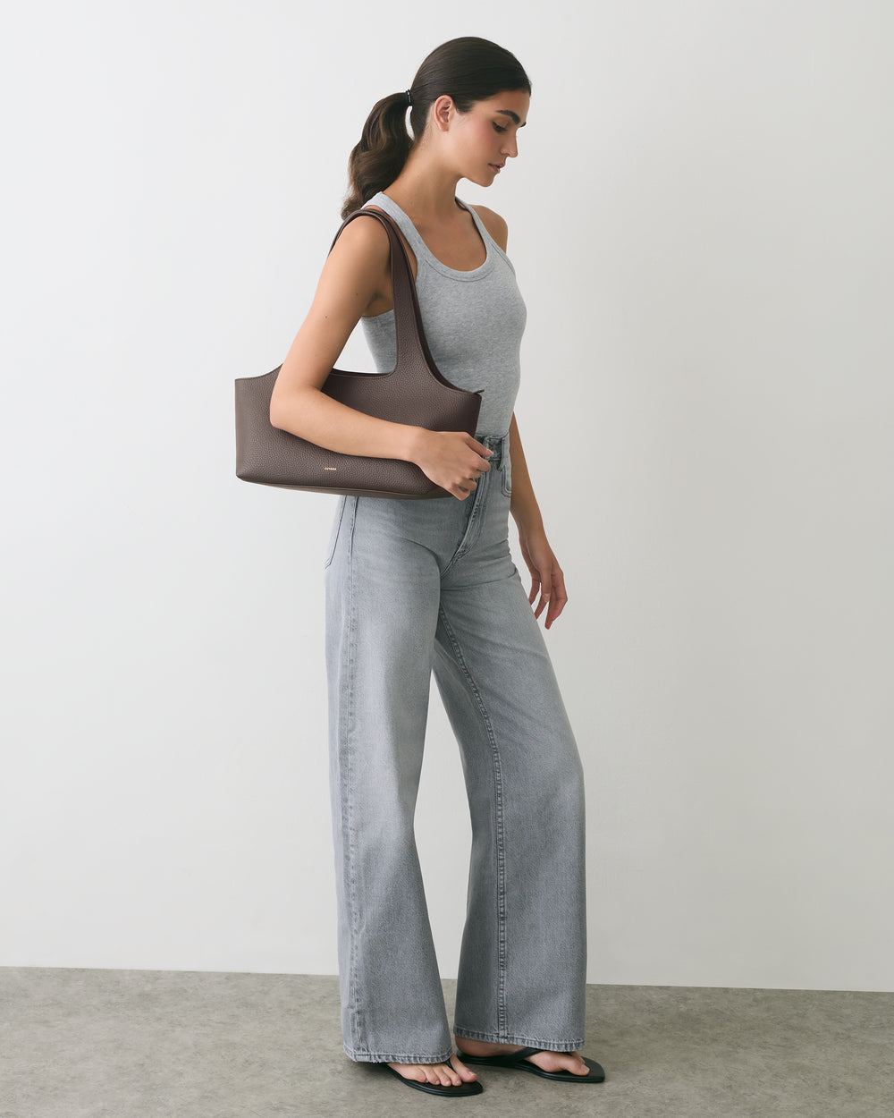 Person in tank top and jeans holding shoulder bag, standing sideways.