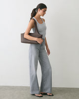 Person in tank top and jeans holding shoulder bag, standing sideways.