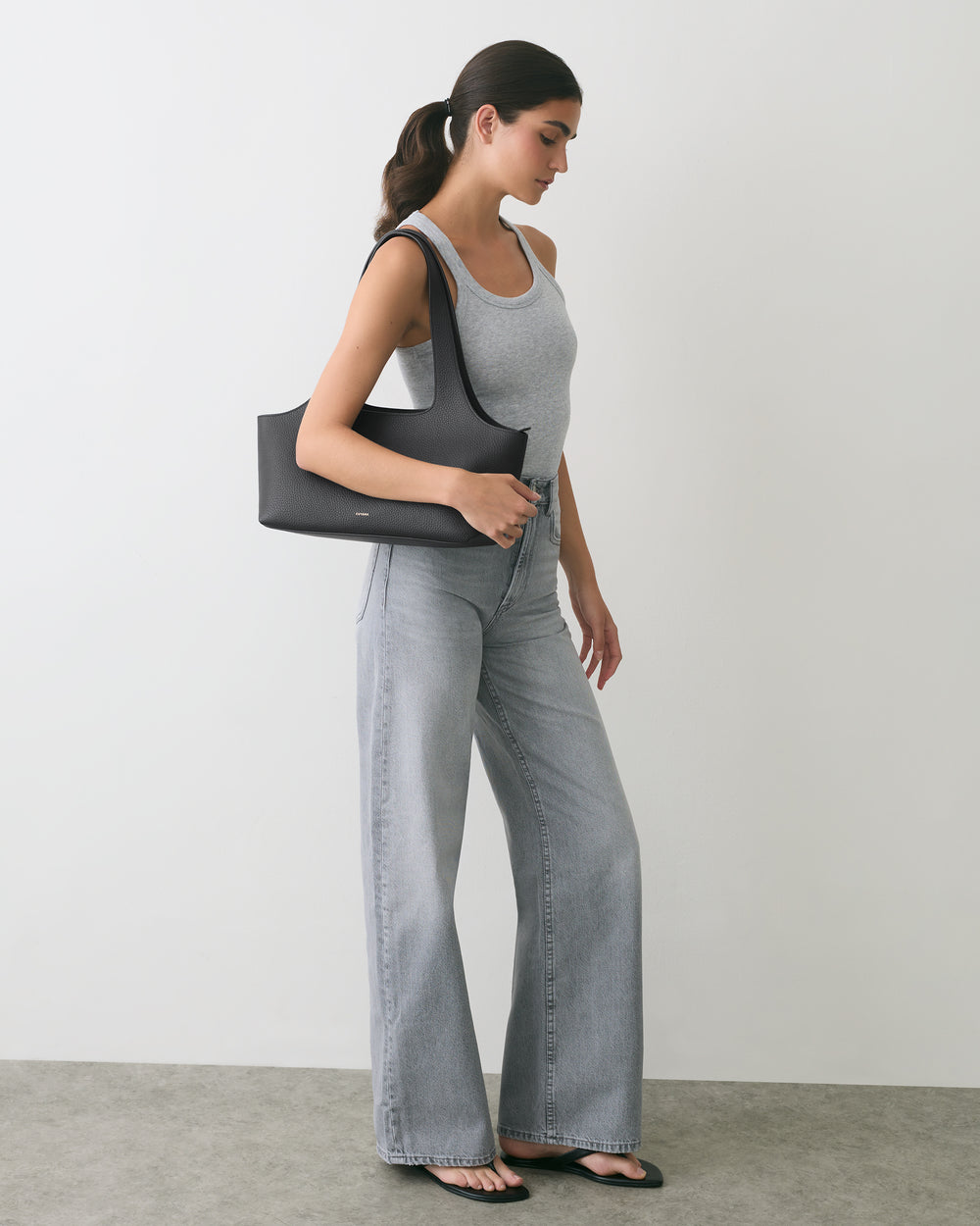 Person in tank top and jeans holding a shoulder bag, standing sideways.