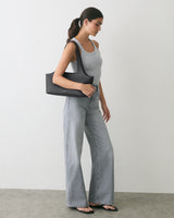 Person in tank top and jeans holding a shoulder bag, standing sideways.