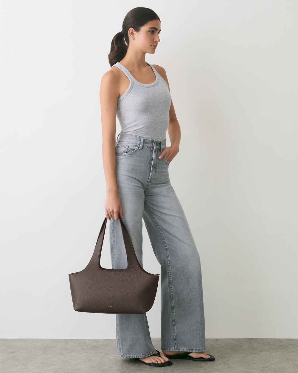 Person standing with handbag, wearing a tank top and wide-leg jeans