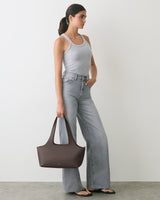 Person standing with handbag, wearing a tank top and wide-leg jeans