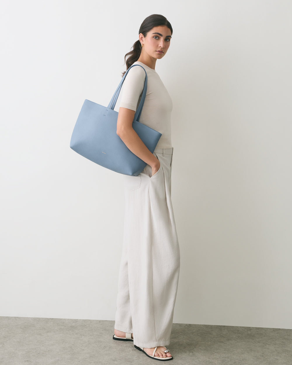 Person standing with a shoulder bag and wearing sandals.