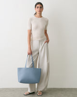 Person wearing a short-sleeve top and wide-leg pants, holding a large tote bag.