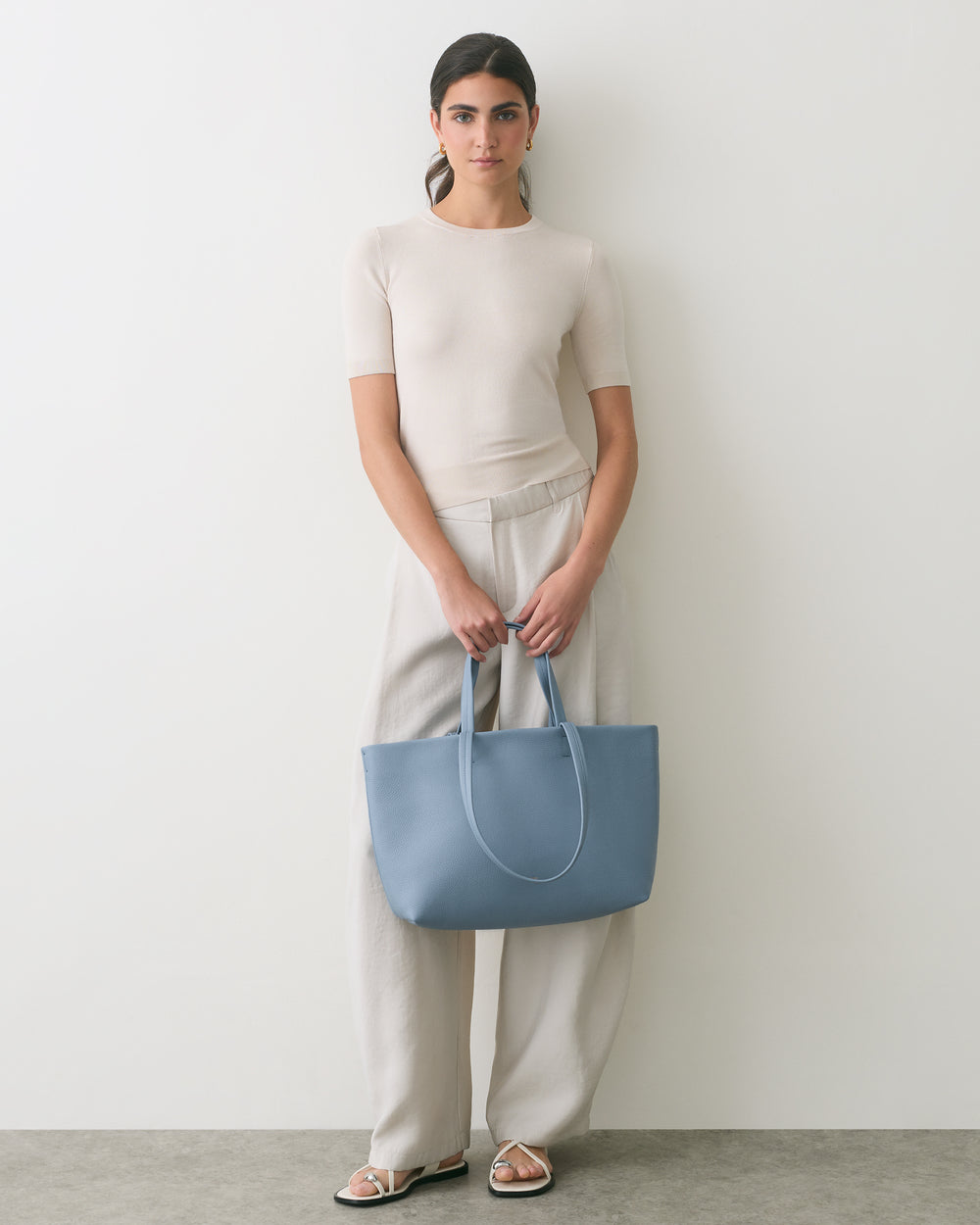 Person holding a large tote bag, wearing a short-sleeve top and wide-legged pants.