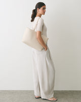 Person standing, holding a large shoulder bag, wearing a short-sleeve top and loose pants.
