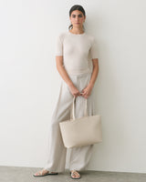Person standing with a handbag wearing a short-sleeve shirt and wide-leg pants.