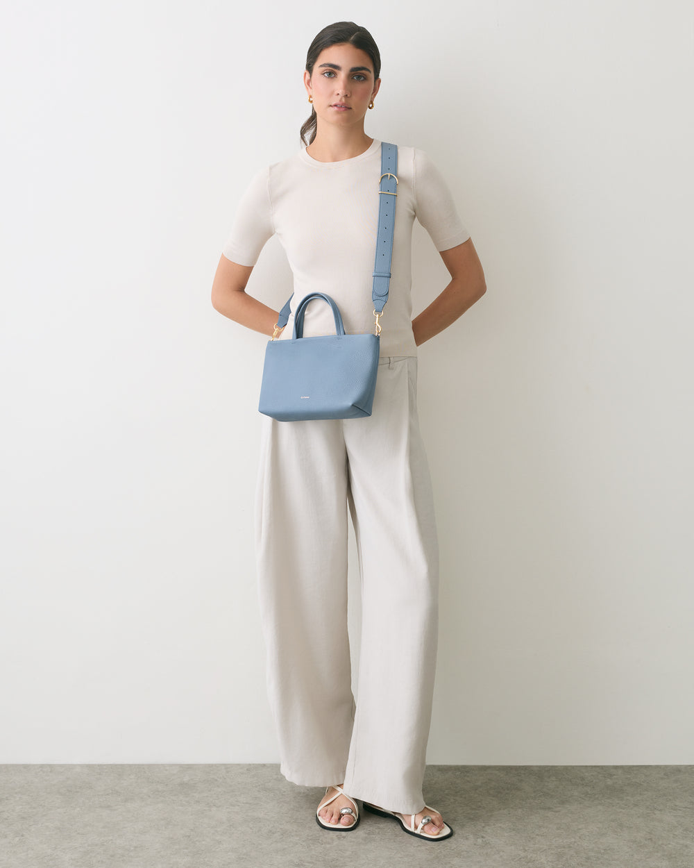 Person in wide-leg pants with shoulder bag, standing against plain wall.