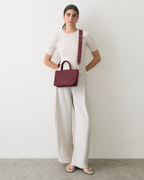 Person standing with crossbody bag and relaxed-fit pants.