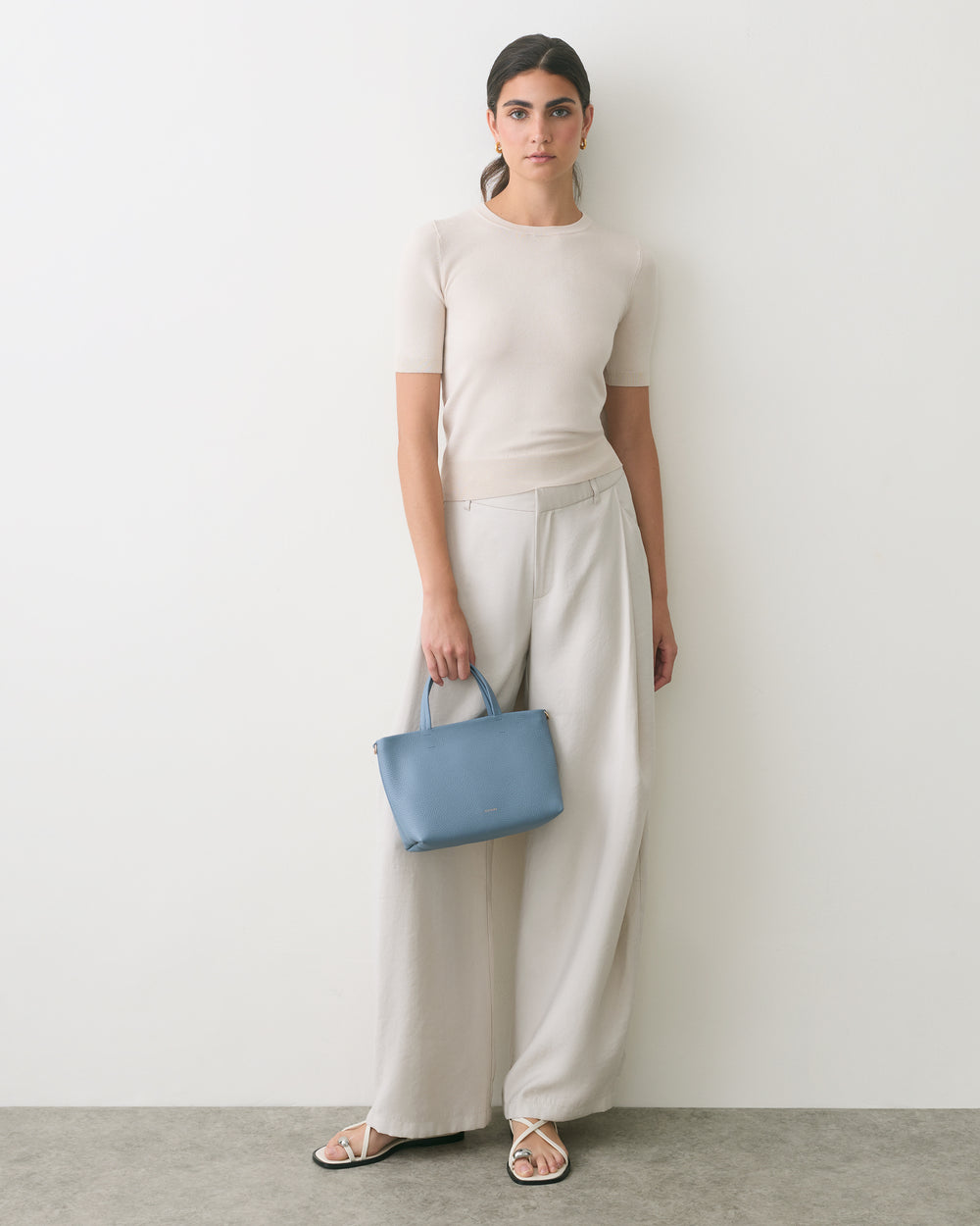 Person standing with a small handbag wearing a short-sleeve top and wide-leg pants.