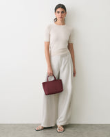Person stands against wall holding a handbag wearing a short-sleeve shirt and wide-leg pants.