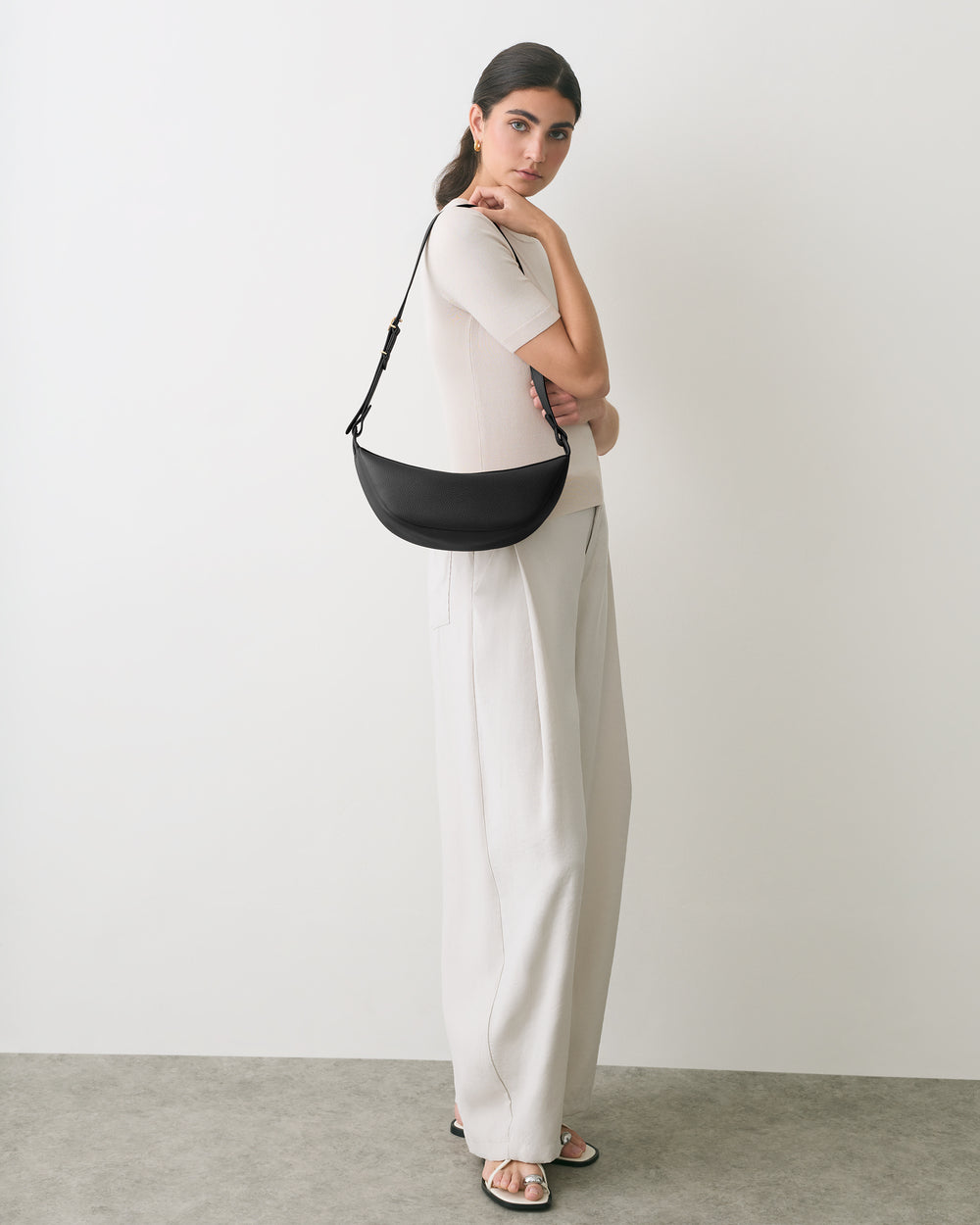 Person standing with a shoulder bag, wearing a shirt and pants.