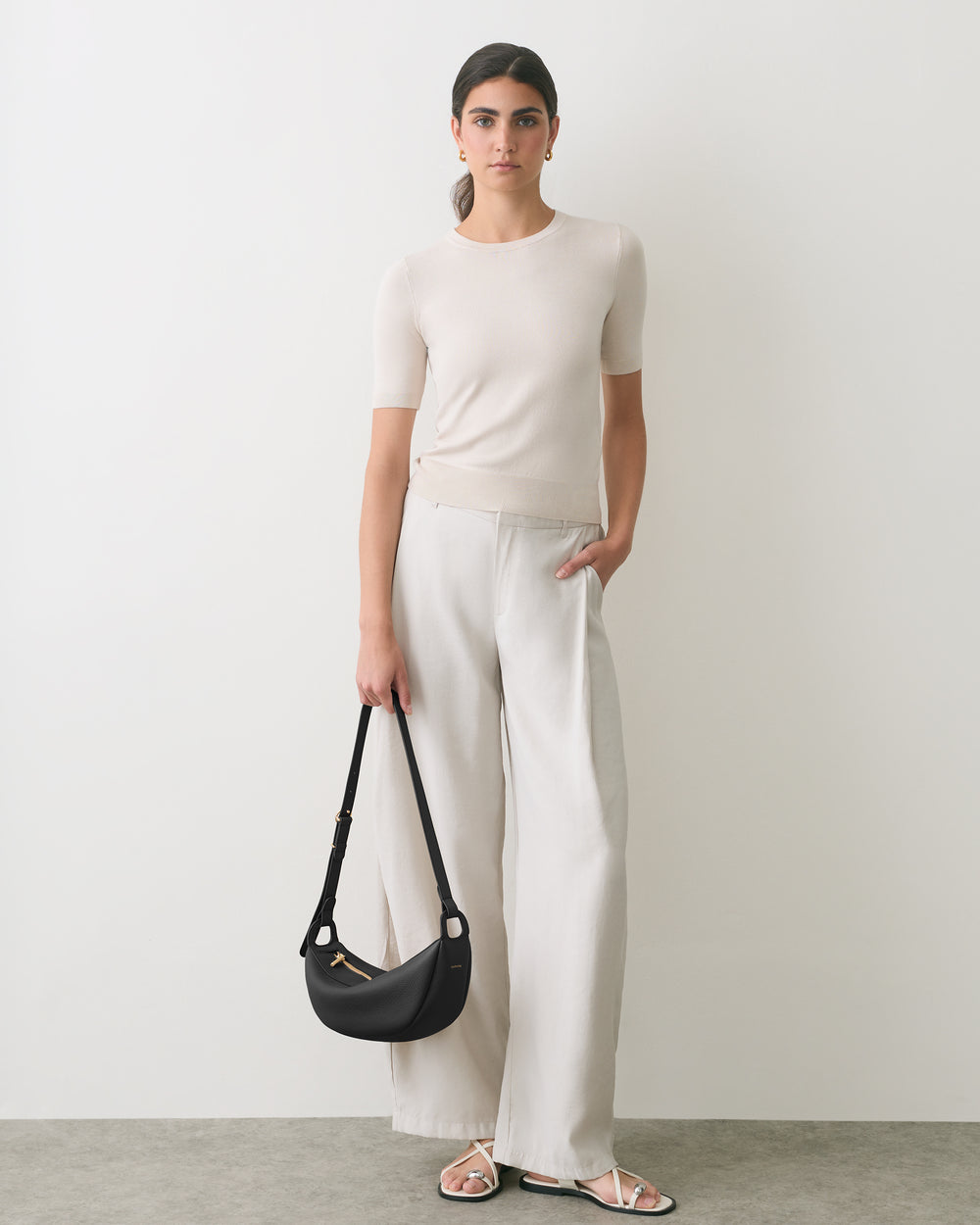 Person standing with handbag wearing short-sleeve shirt and wide-leg pants.